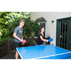 Two people play outdoors with JOOLA Linus Outdoor Table Tennis Rackets on a blue table.