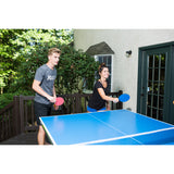 Two people play outdoors with JOOLA Linus Outdoor Table Tennis Rackets on a blue table.
