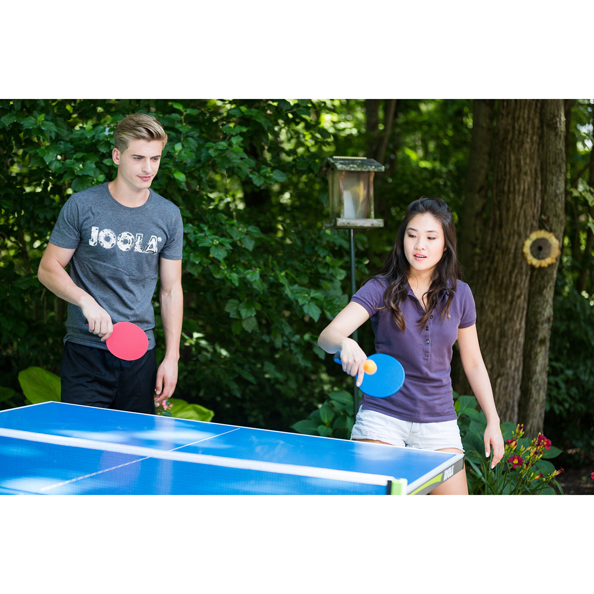 Two people playing outdoor table tennis with the JOOLA Linus Outdoor Table Tennis Racket.