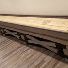 The Champion Rustic 9' Shuffleboard Table by Champion stands on a wood floor near a beige wall.