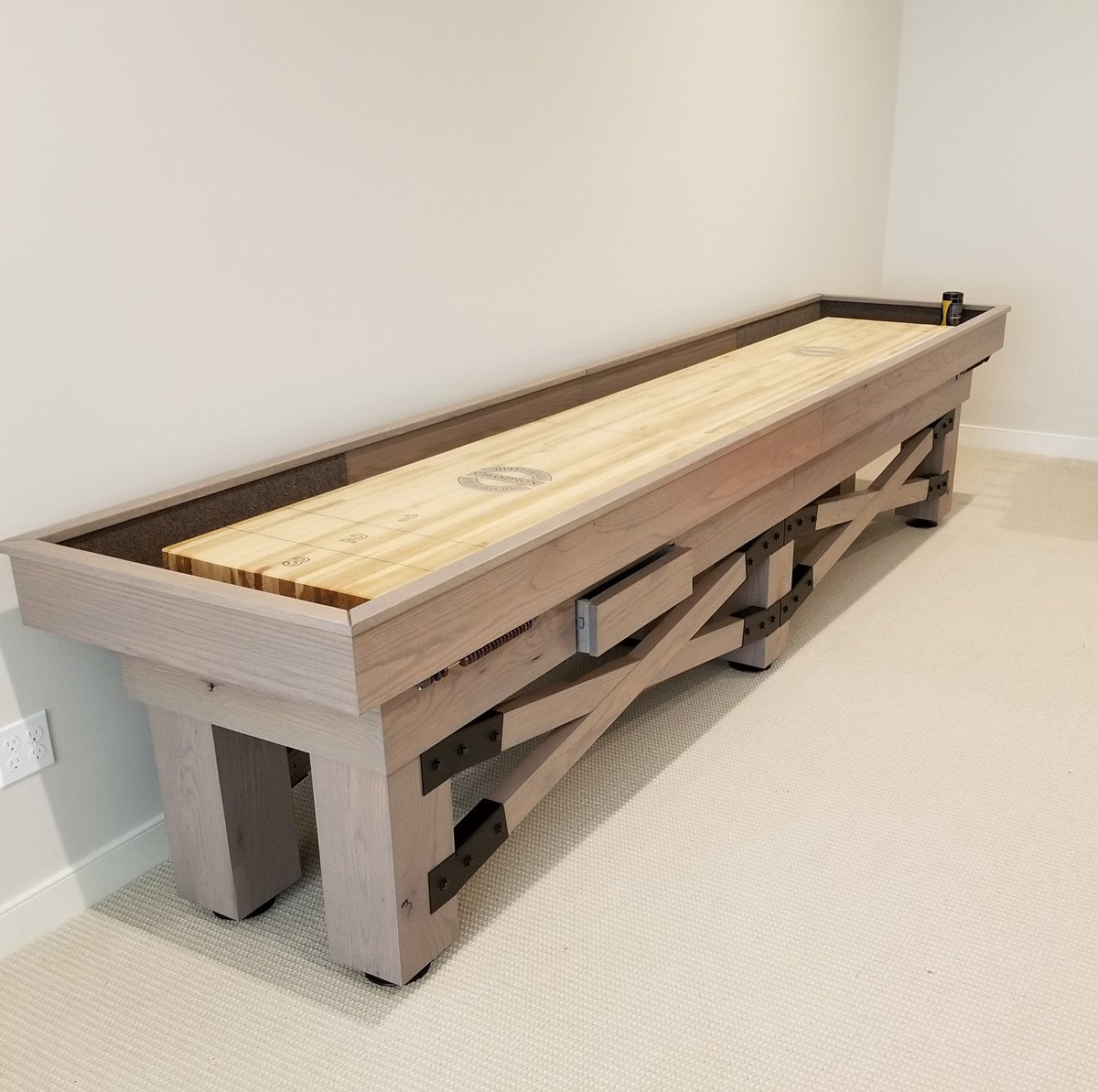 The Champion Rustic 9' Shuffleboard Table by Champion stands against a plain wall on carpet.