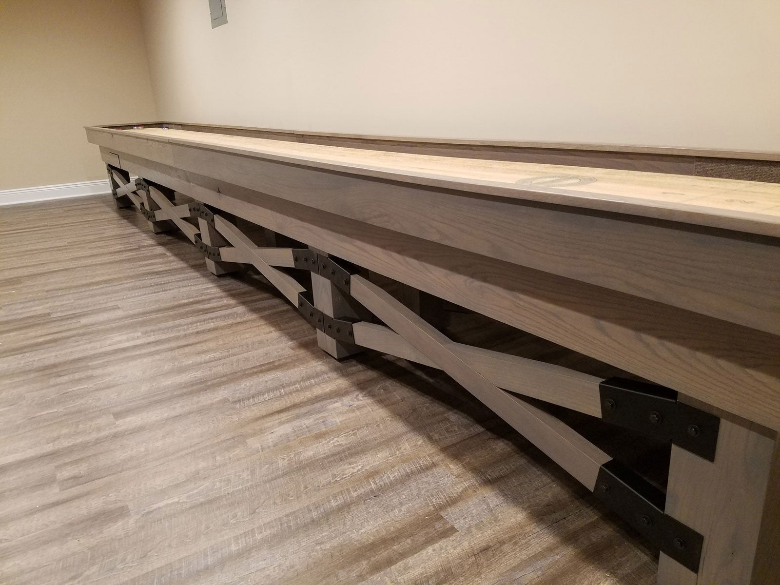 Champion Rustic 9' Shuffleboard Table by Champion stands on wood-patterned flooring.