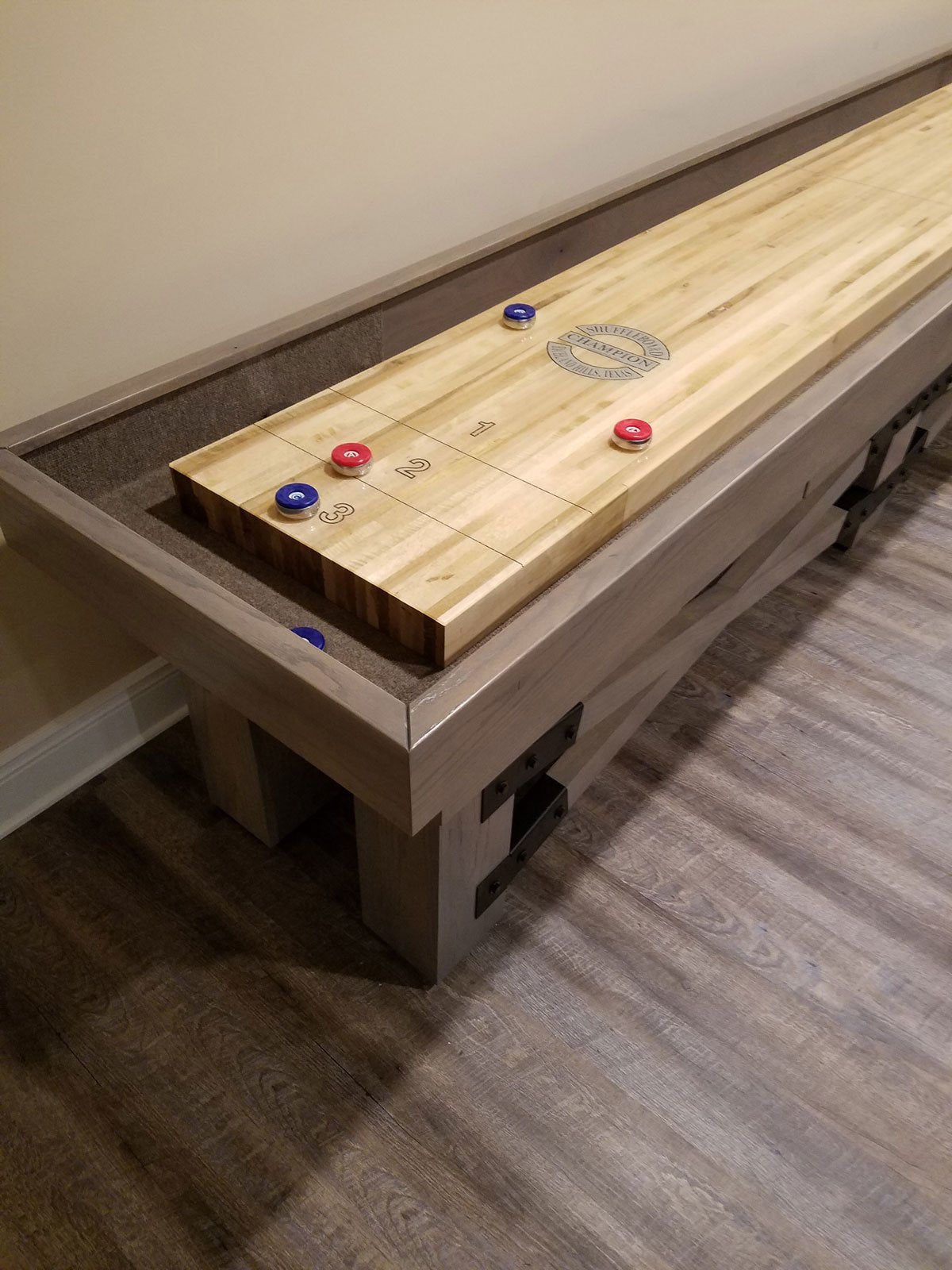 Champion Rustic 9' Shuffleboard Table by Champion with blue and red pucks on maple playfield.