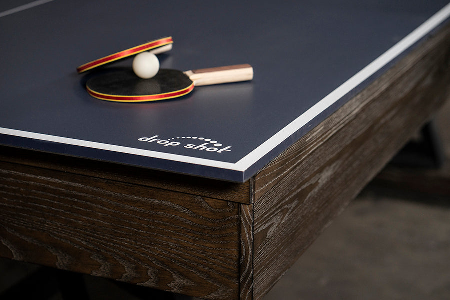 Two paddles and a ball on a Nixon CrissyCross 7' pool table by Nixon Billiards in charcoal.