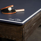 Two paddles and a ball on a Nixon CrissyCross 7' pool table by Nixon Billiards in charcoal.