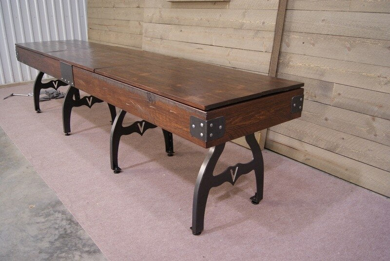 Venture Williamsburg 12' Shuffleboard Table with metal legs on carpet, by a wooden wall.