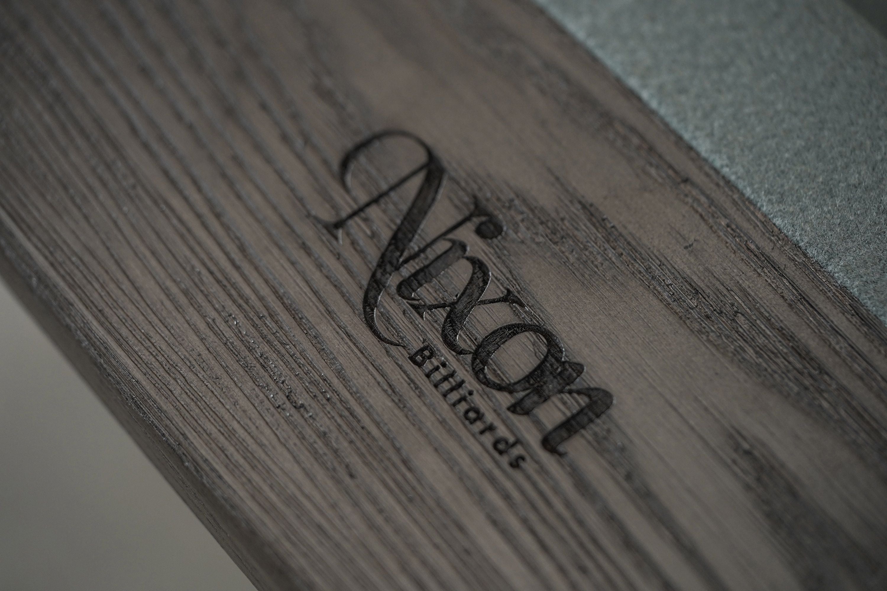 Close-up of a Nixon Birdy 7' Slate Pool Table in Grayson Grey’s wooden surface with engraved logo.