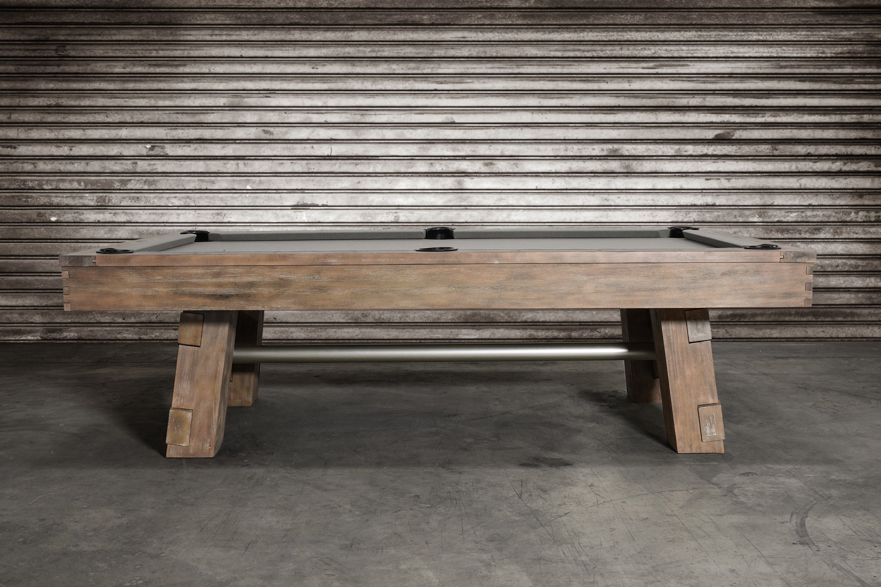 The Nixon Georgia 8' Slate Pool Table by Nixon Billiards sits on a concrete floor by a metal wall.