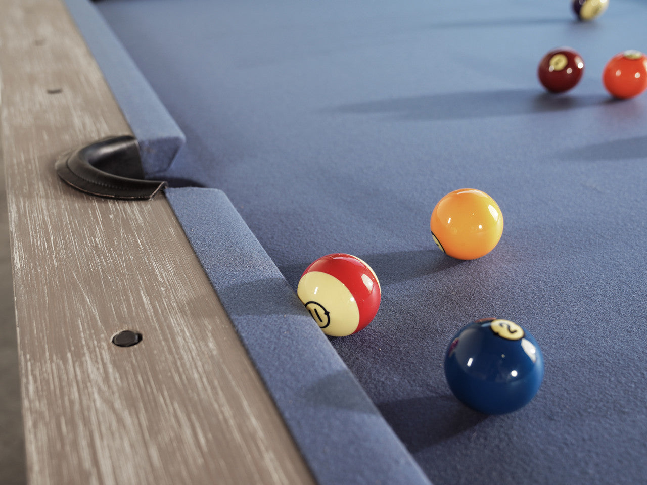 Three billiard balls rest near a pocket on a Nixon Huck 7' Slate Pool Table in Grey White Oak.