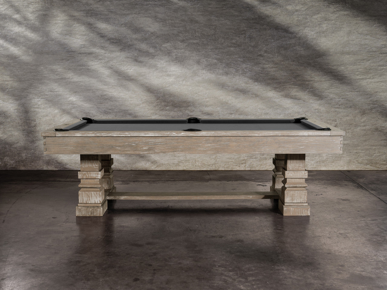 A Nixon Huck 7' Slate Pool Table in Grey White Oak rests on a concrete floor.