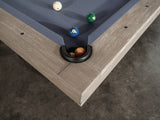 Corner of a Nixon Huck 7' Slate Pool Table in Grey White Oak by Nixon Billiards, balls in pocket.