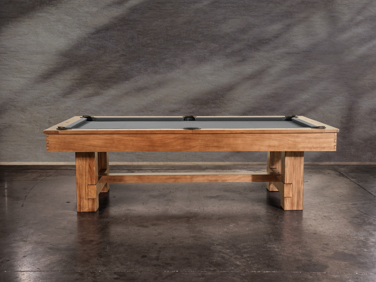 The Nixon Presli 7' Slate Pool Table in Native Acacia finish sits on a concrete floor.