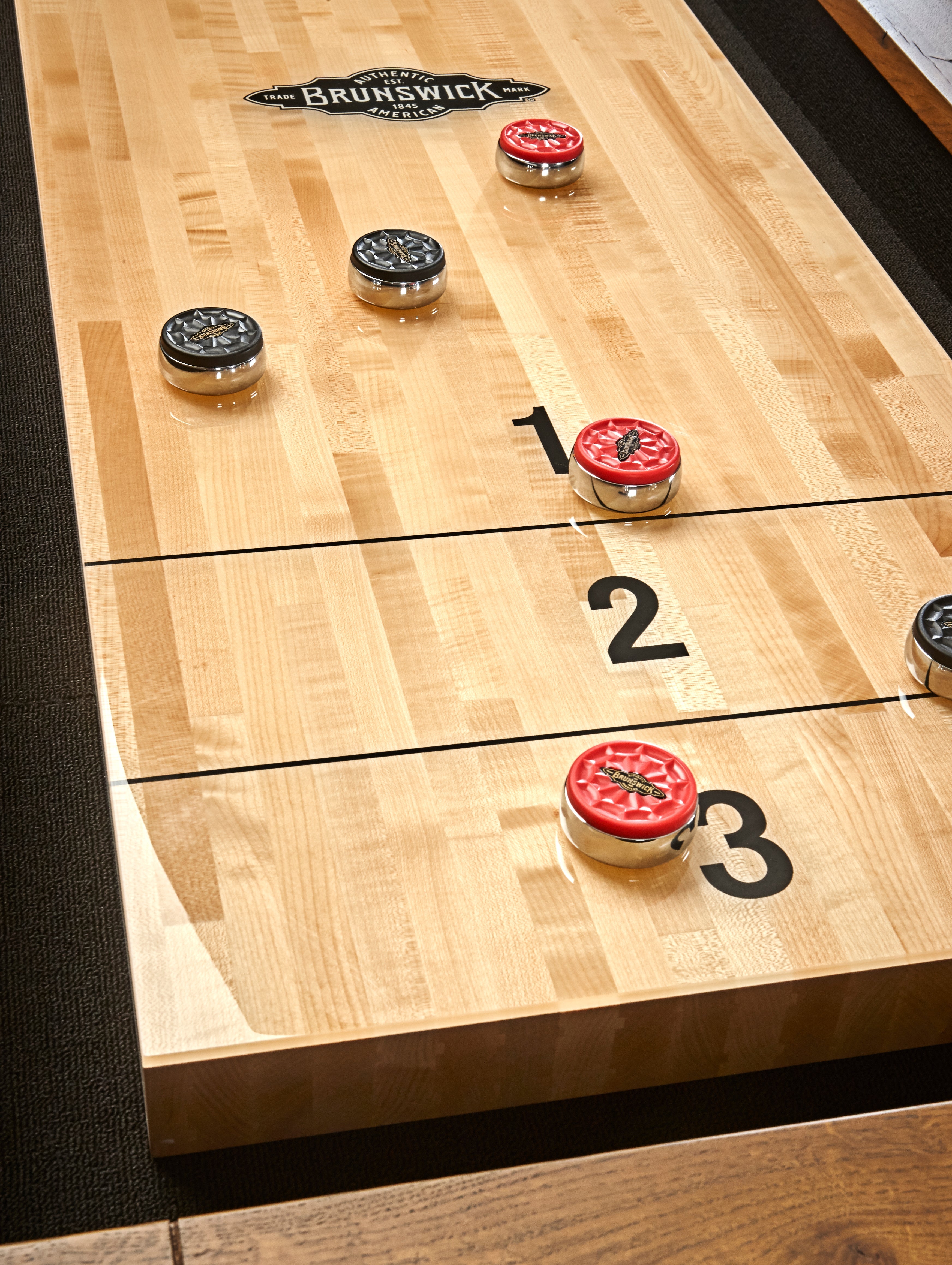 Brunswick Billiards Parsons 12' Shuffleboard Table with black and red pucks on zones 1–3.