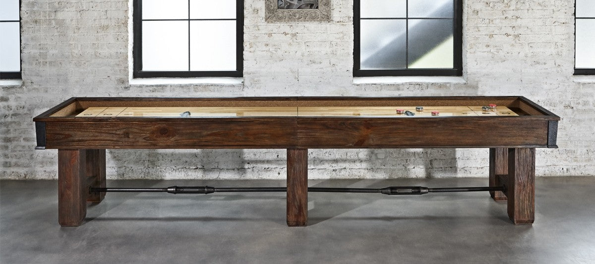 A Brunswick Canton 14' Shuffleboard Table in Black Forest sits before windows in a brick-walled room.