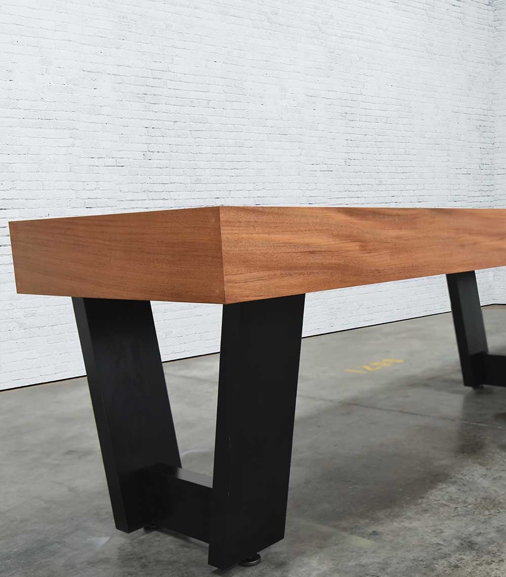 A Venture Monaco 18' Shuffleboard Table with black metal legs sits on a concrete floor.