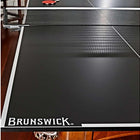 A Brunswick Billiards OAKLAND II 8' Pool Table stands on a wood floor, cues and balls ready.