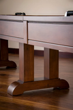 Close-up of an American Heritage Billiards Milan 14' Shuffleboard Table leg on hardwood floor.
