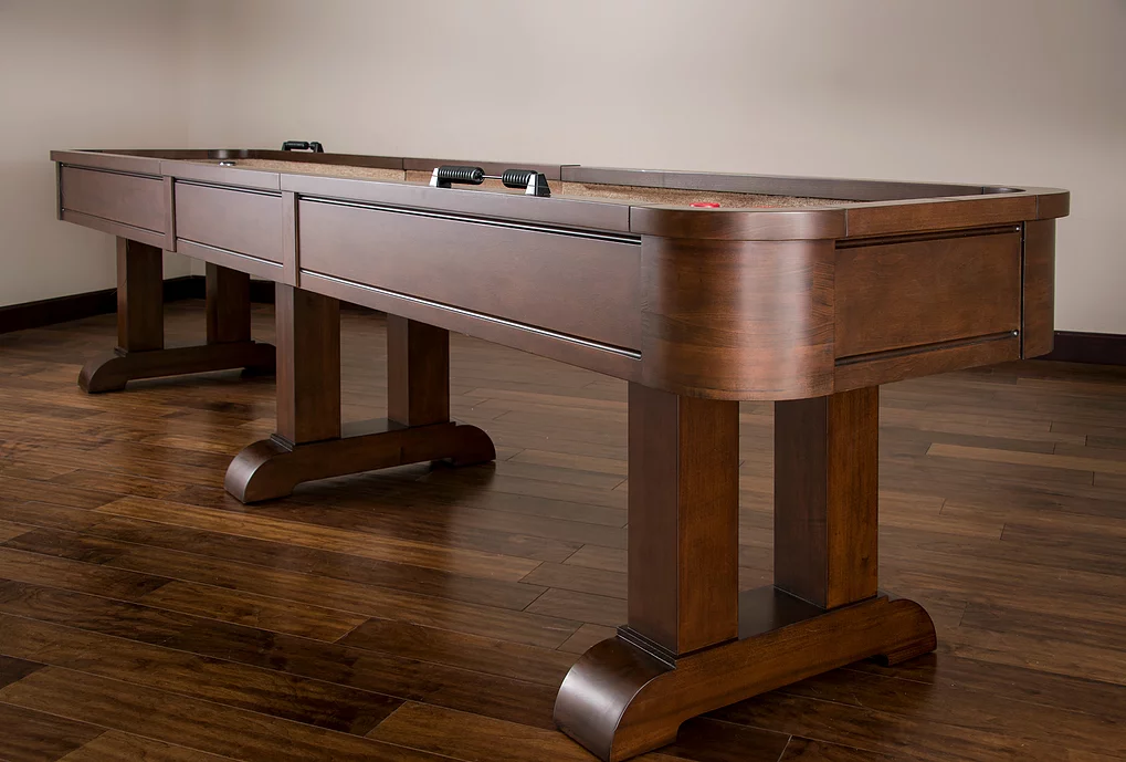 The American Heritage Billiards Milan 14' Shuffleboard Table in Navajo stands against a wall.