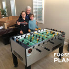 Three people behind a Tornado T-3000 Foosball Table in a living room with moving boxes.