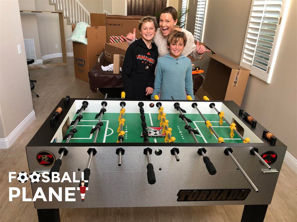 A woman and two kids stand by a Tornado T-3000 Foosball Table (Silver Coin) in a living room.