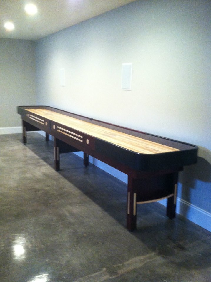The Champion 9' The Grand Champion Shuffleboard Table stands against a blank wall on polished floors.