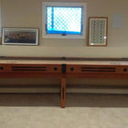 A Champion 9' The Grand Champion Shuffleboard Table sits beneath three windows in the room.