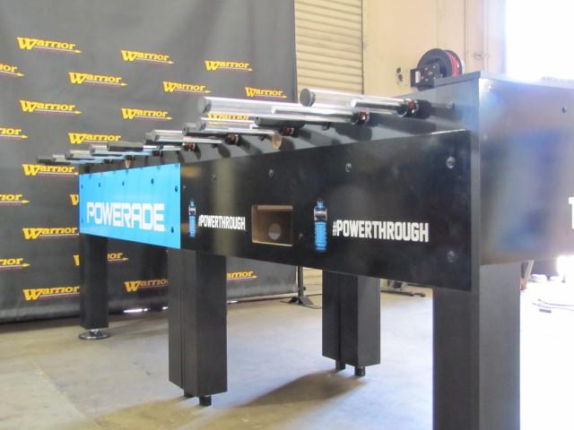 Warrior 8 Players Foosball Table with split bearing, shown in front of a Warrior banner.