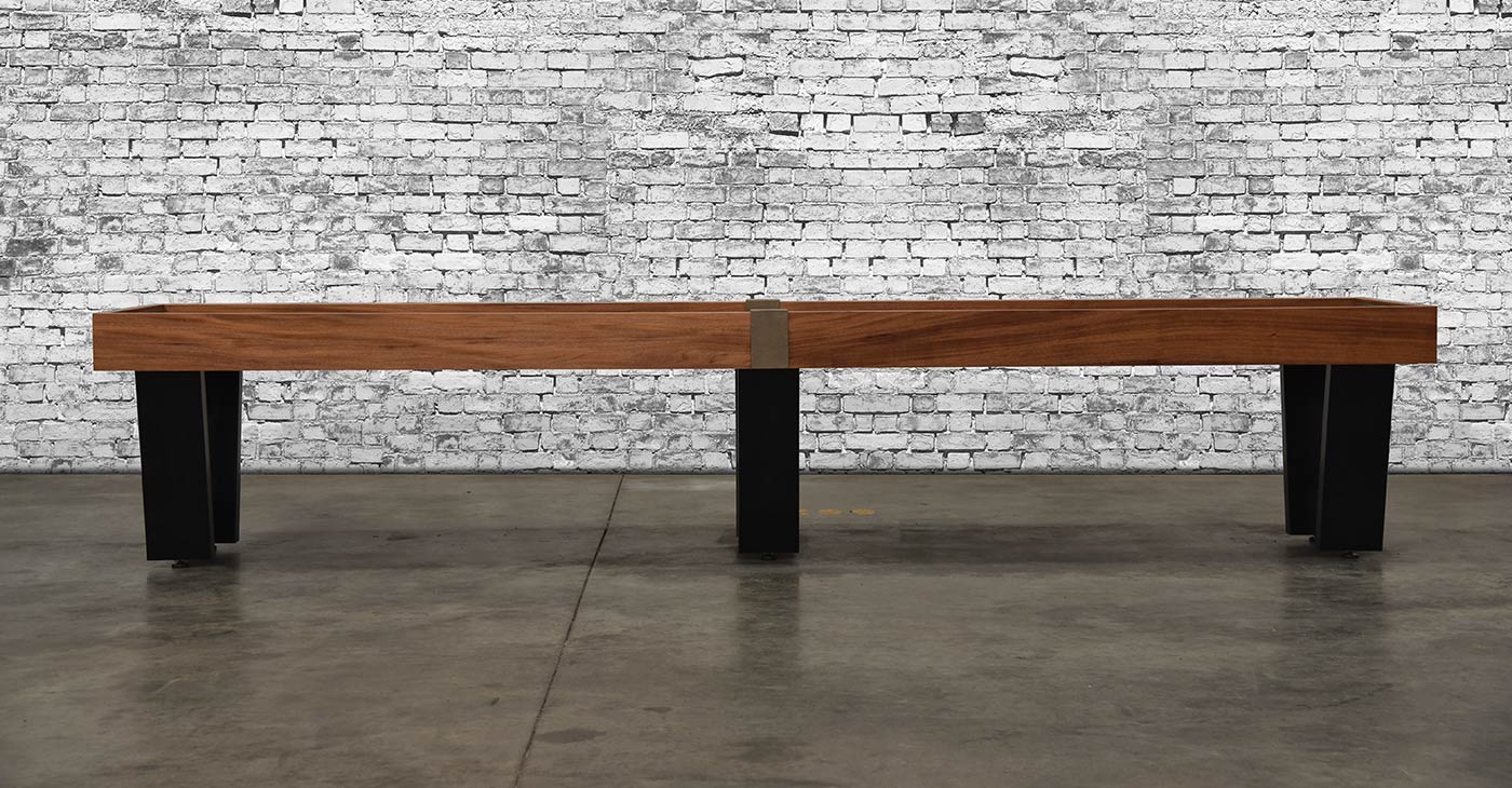 The Venture Monaco 18' Shuffleboard Table by Venture stands against a white brick wall on concrete.
