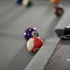A red and white billiard ball rests by a Nixon Birdy 7' Slate Pool Table in Grayson Grey.