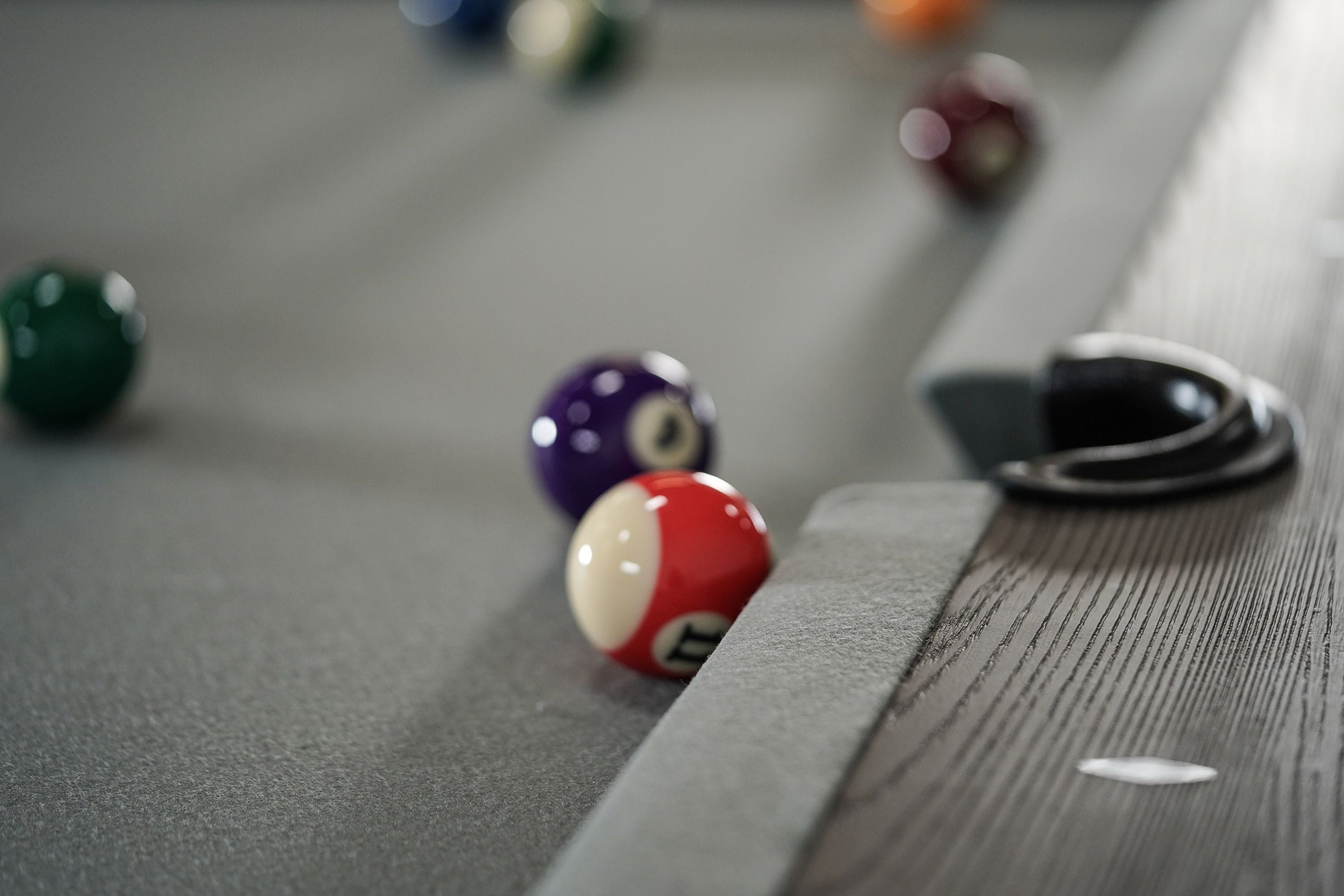 A red and white ball sits by a pocket on a Nixon Birdy 8' Slate Pool Table in Grayson Grey.