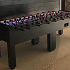 A Warrior 8 Players black foosball table with split bearing is set up on a carpeted floor.