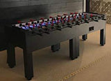 A Warrior 8 Players black foosball table with split bearing is set up on a carpeted floor.